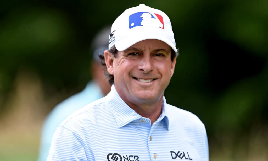 Billy Andrade smiling confidently in golf cap and light blue shirt with blurred green background Wallpaper
