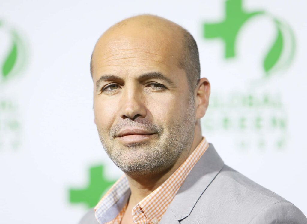Billy Zane confident in sharp suit bright backdrop wallpaper perfect for actor fans background