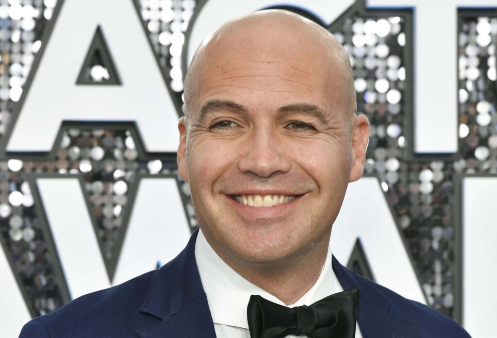 Billy Zane smiling in black tuxedo at public event with sparkling backdrop vibrant wallpaper background
