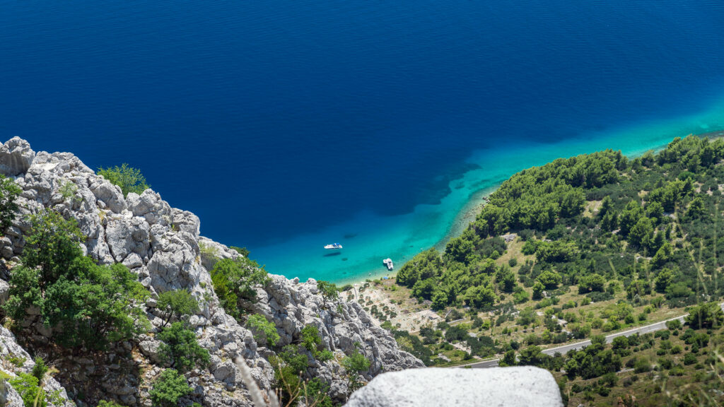 Biokovo Mountain Range Croatia with rocky cliffs vibrant turquoise Adriatic Sea and coastal boats Wallpaper