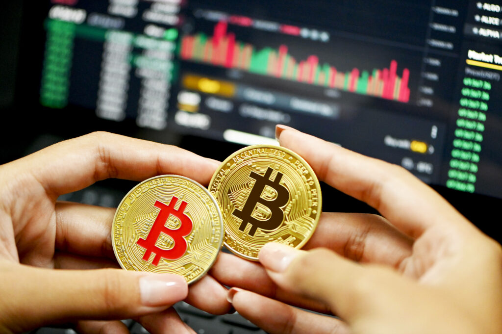 Two cryptocurrency coins with Bitcoin logo held before digital trading screen showing charts and data Wallpaper