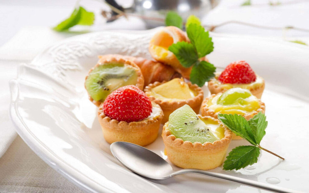 Mouthwatering Fruit Tart Garnished with a Fresh Mint Leaf: A Delightful Bite-sized Treat Wallpaper