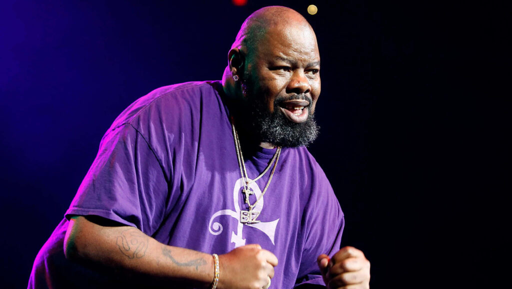 Biz Markie performing energetically on stage in vibrant purple shirt under bright spotlight wallpaper
