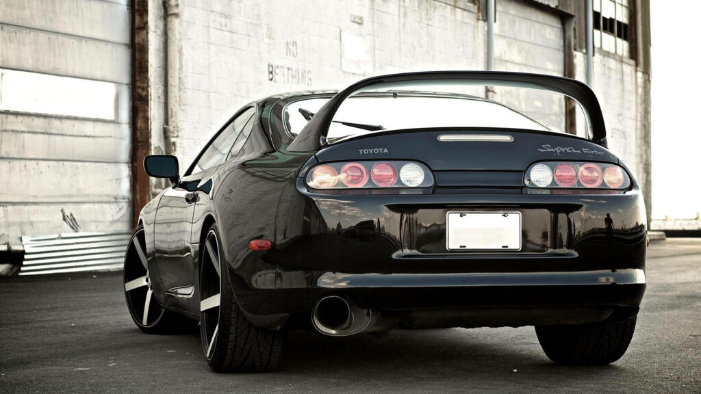 Rear view of black 1994 Toyota Supra Mk4 with iconic tail lights and large rear wing parked outdoors Wallpaper