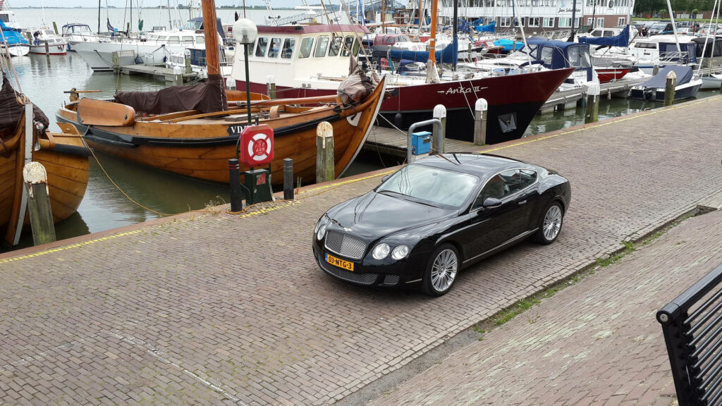 Sleek Black Bentley Continental GT Navigating the Seaside Harbor Wallpaper