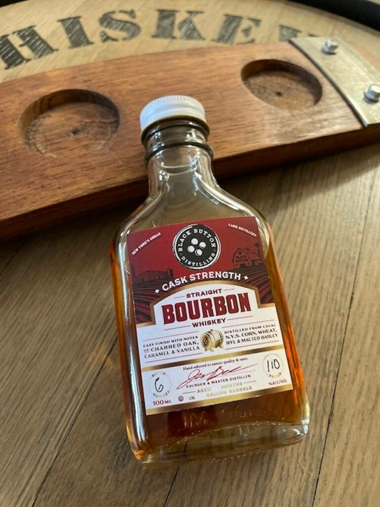 Close-up of Black Button Distilling Cask Strength Bourbon bottle on rustic wooden surface wallpaper