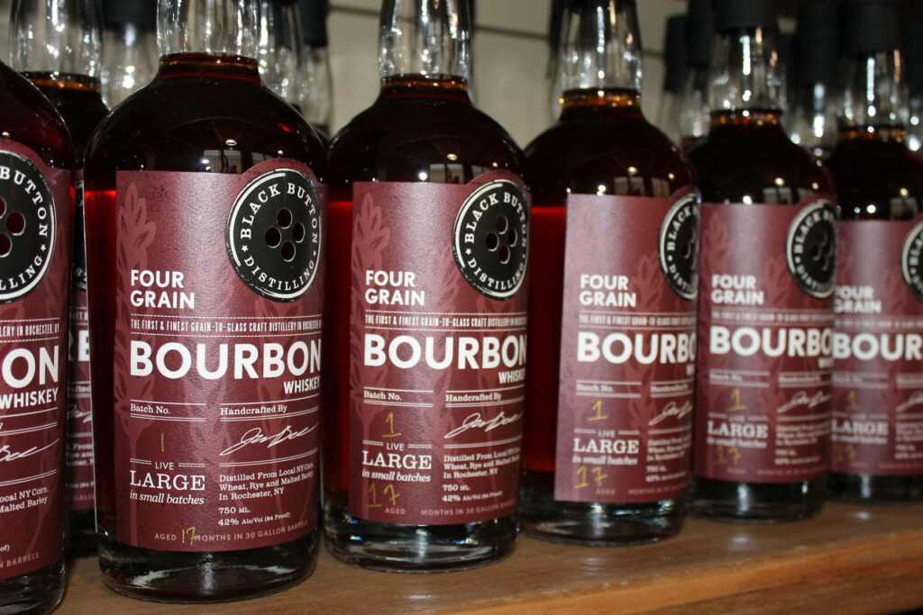 Black Button Distilling Four Grain Bourbon bottles lined up with amber color and Rochester labels Wallpaper