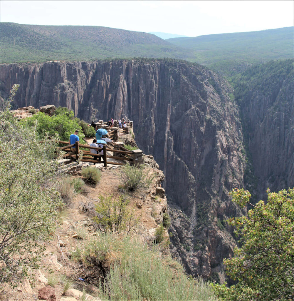 Visitors admiring stunning Black Canyon cliffs and lush greenery under a clear sky background Wallpaper