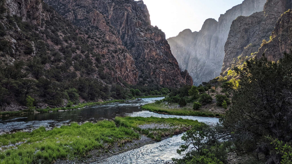 Black Canyon rugged cliffs over winding river sunlight streaming lush greenery natural landscape Wallpaper