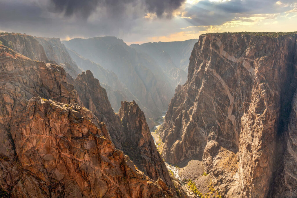 Black Canyon sheer cliffs rugged rock formations golden sunlight moody sky wallpaper background