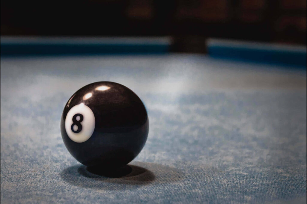 Close-up of black eight-ball on textured blue pool table with moody background in sharp focus Wallpaper