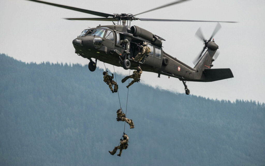 Soldiers rappelling from Black Hawk helicopter over dense forest during tactical military operation Wallpaper