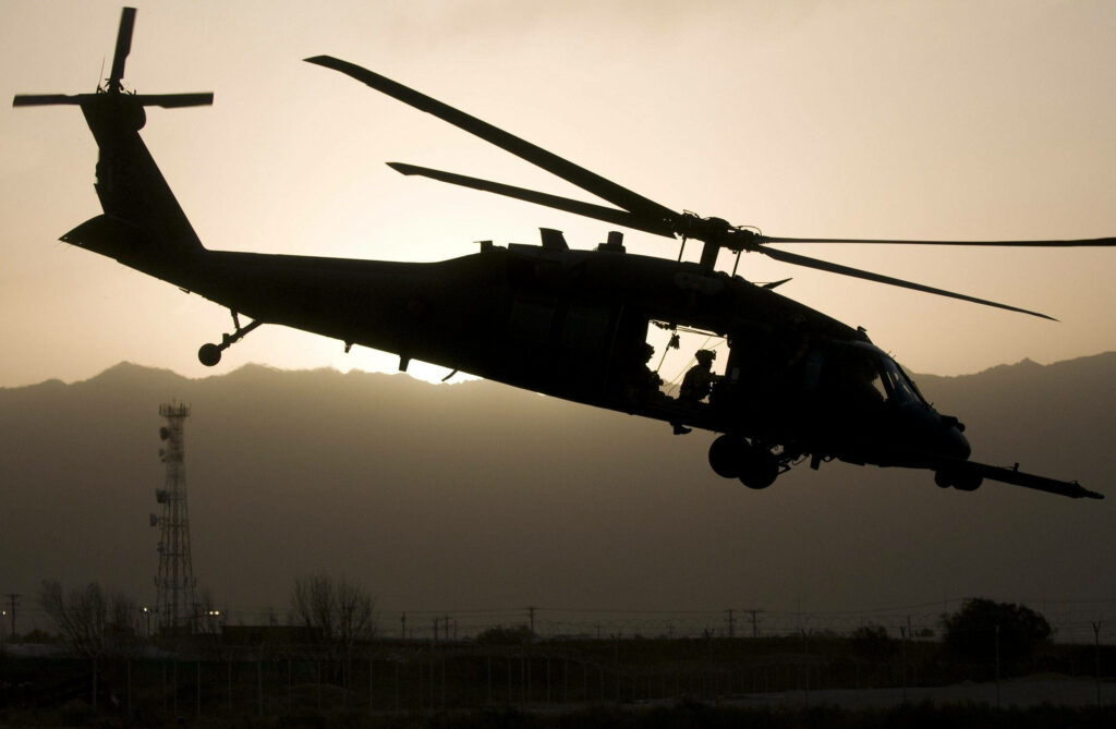 Black Hawk helicopter hovering over rugged terrain at dusk silhouetted by setting sun combat aid Wallpaper