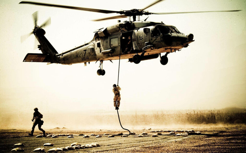 Black Hawk helicopter hovering with soldier rappelling and companion against dusty sky wallpaper