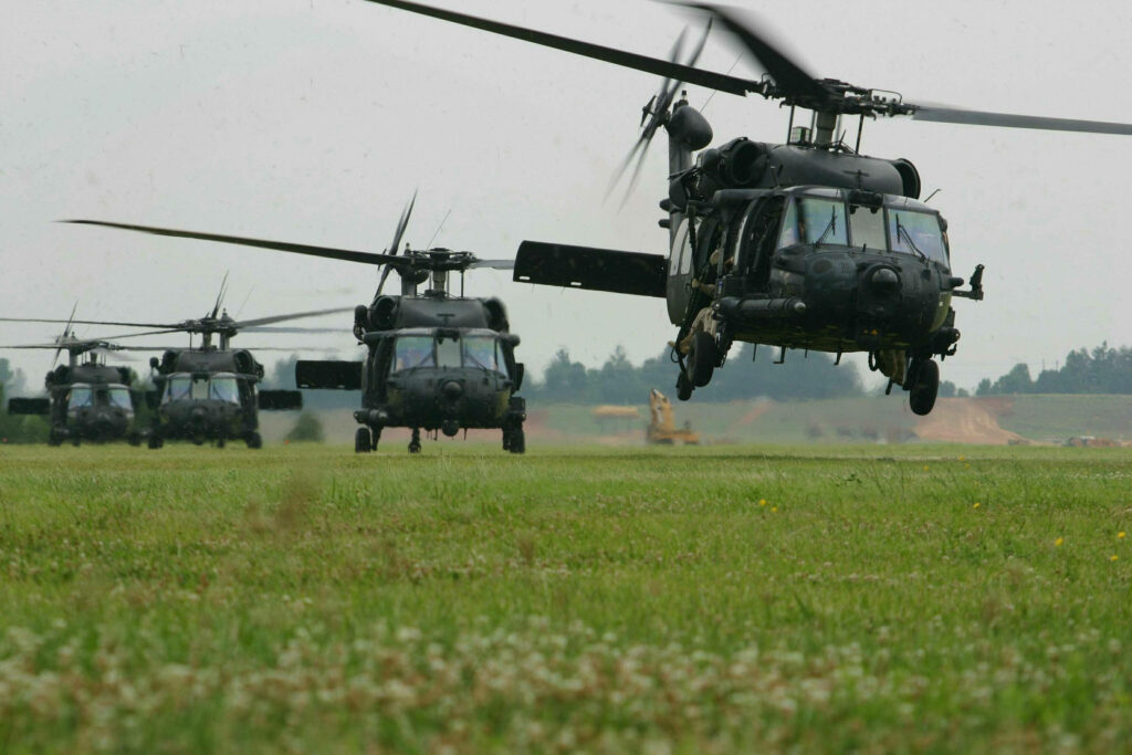 Black helicopters flying in tight formation over grassy field showcasing teamwork and precision Wallpaper