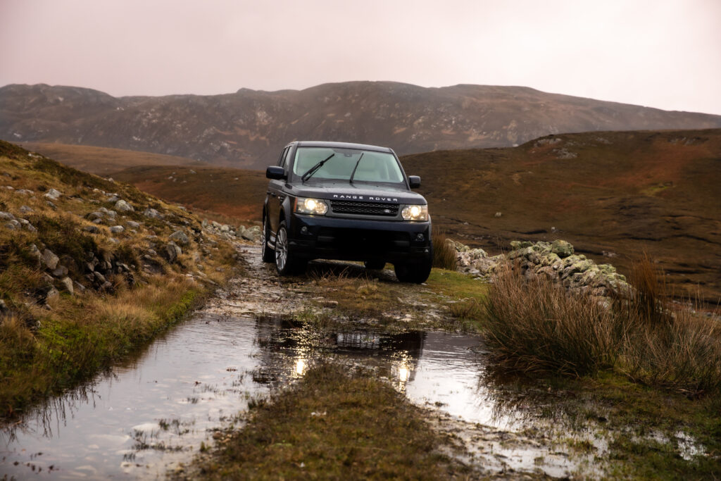 Black Land Rover SUV in Rugged Wet Landscape Wallpaper Background