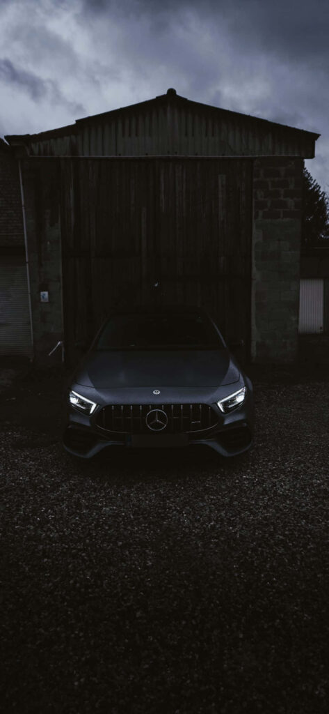 Front view of black Mercedes AMG with bold headlights against dark rustic wallpaper background