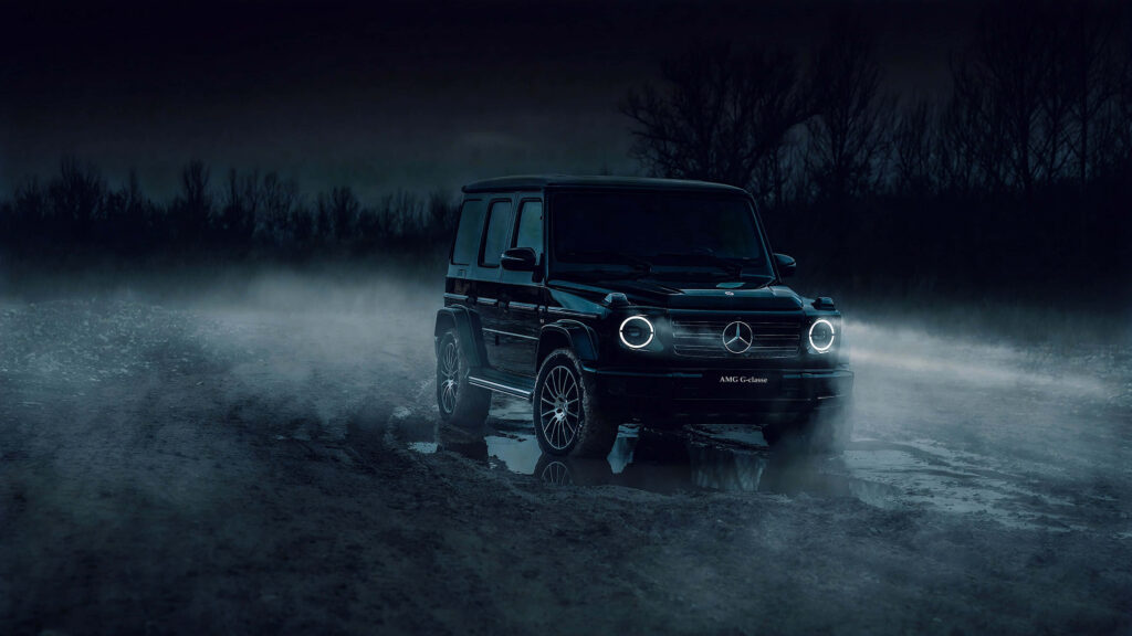 Black Mercedes AMG G-Class with glowing headlights on misty rugged terrain at night wallpaper