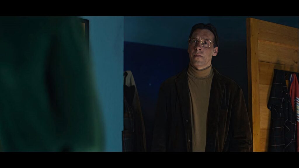 Black Mirror Scene: Man in Eyeglasses, Brown Jacket, Dimly Lit Room Wallpaper