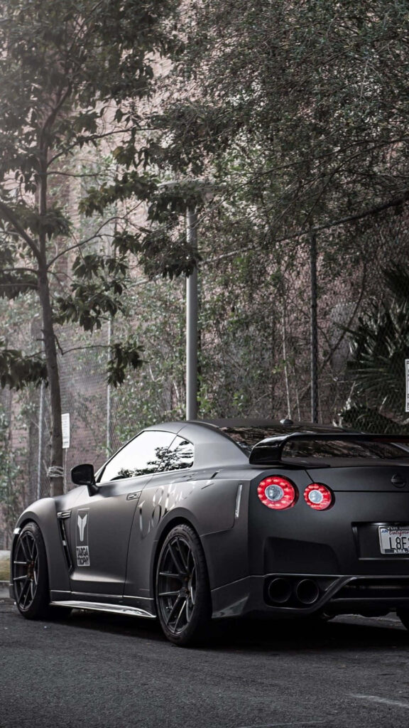 Black Nissan GTR R35 parked with sleek lines aggressive stance custom details urban greenery background Wallpaper