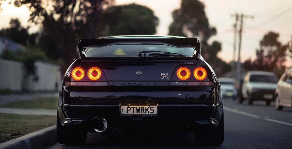 Rear view of black Nissan Skyline R33 GT-R with iconic tail lights and spoiler at dusk street Wallpaper