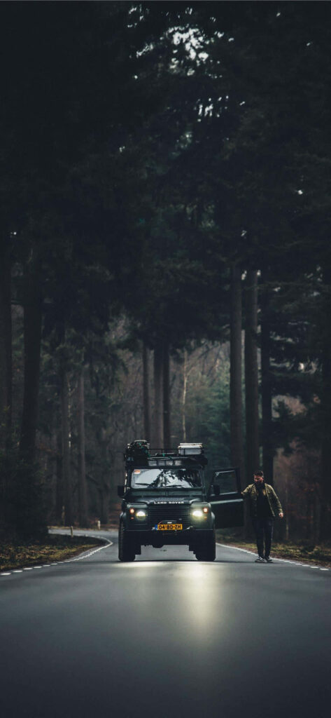 Black Range Rover parked on forest road with person beside open door under overcast sky wallpaper
