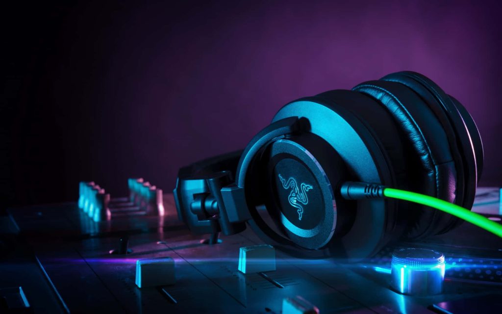 Black Razer gaming headphones on audio mixer with neon blue and purple lighting wallpaper