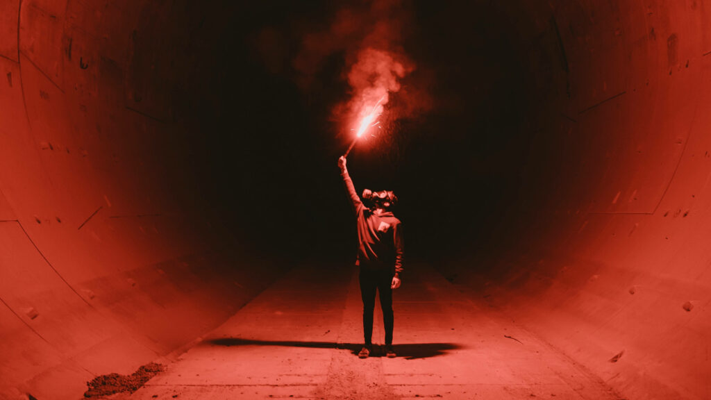 Apocalyptic Vibes: Man Brandishing Red Flare in Eerie Tunnel - 4K Black and Red Wallpaper