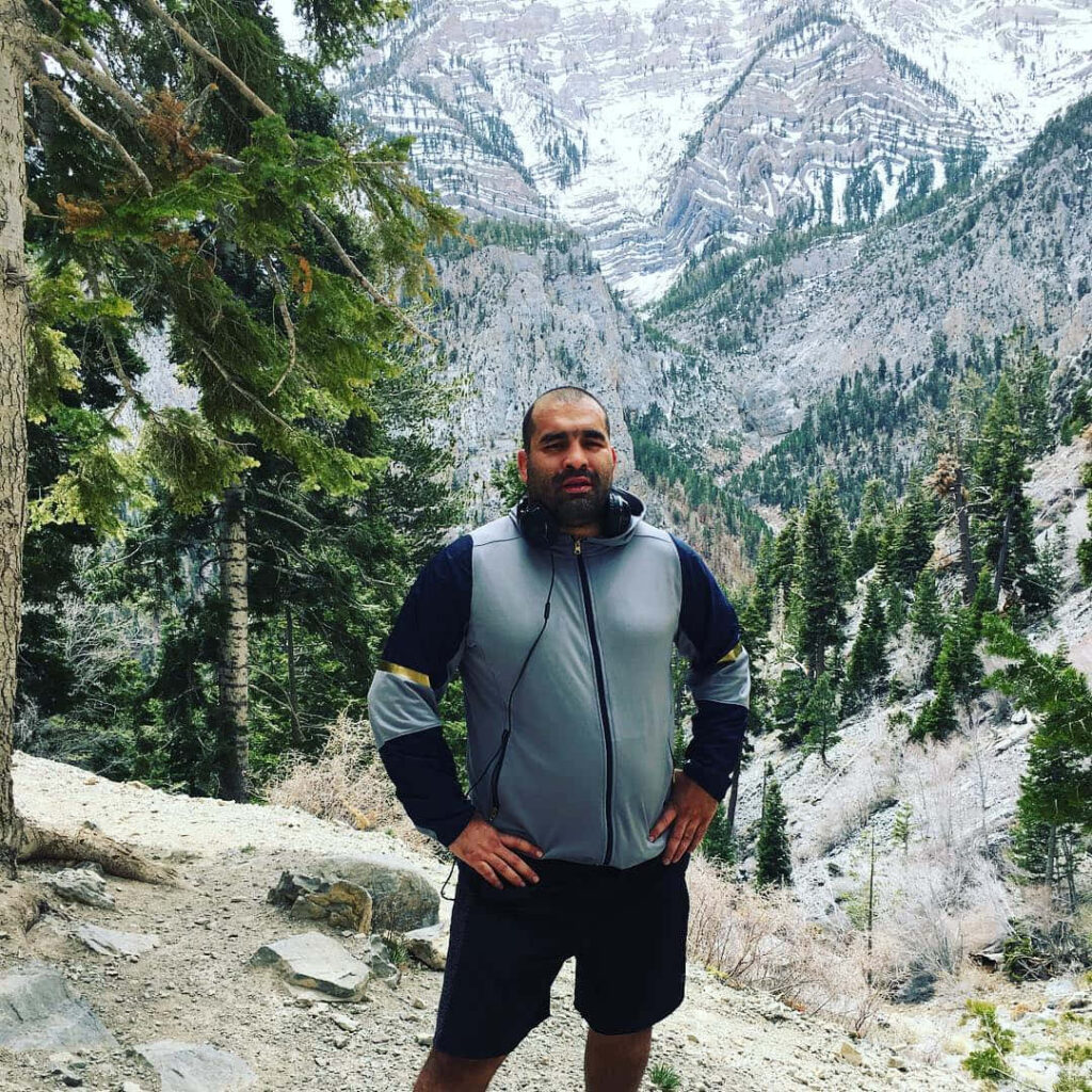 Blagoy Ivanov on rugged mountain path with pine trees and snow-dusted peaks wilderness adventure Wallpaper