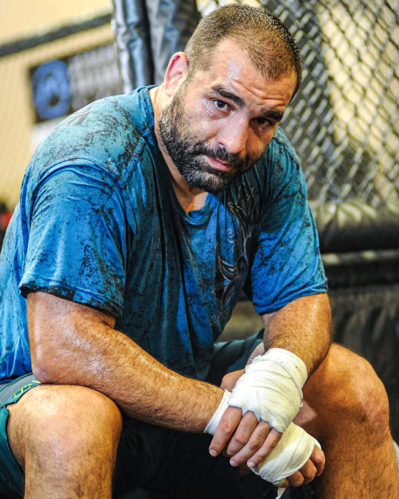 Blagoy Ivanov resting against cage sweat soaked focused after intense MMA training session wallpaper