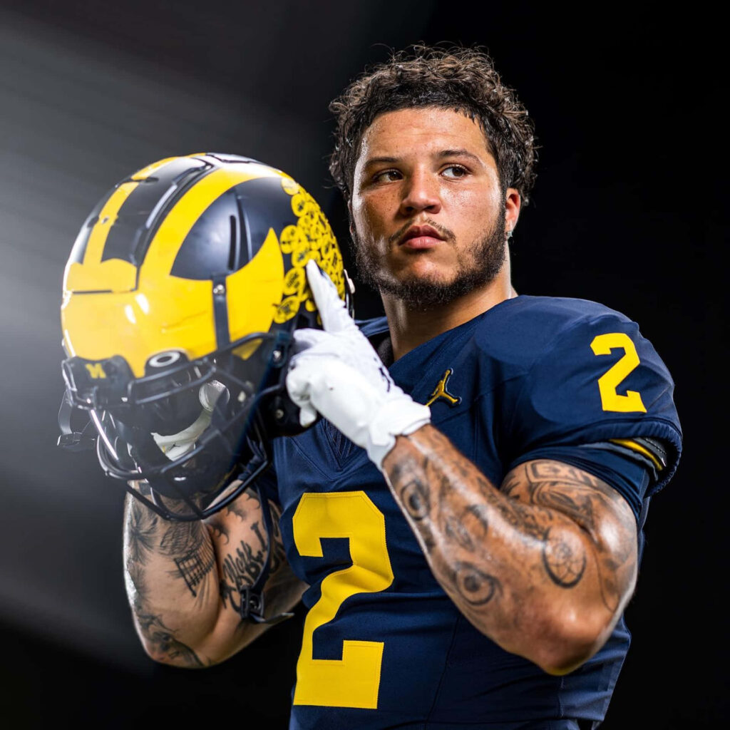 Blake Corum in football uniform holding helmet with determined expression striking portrait wallpaper