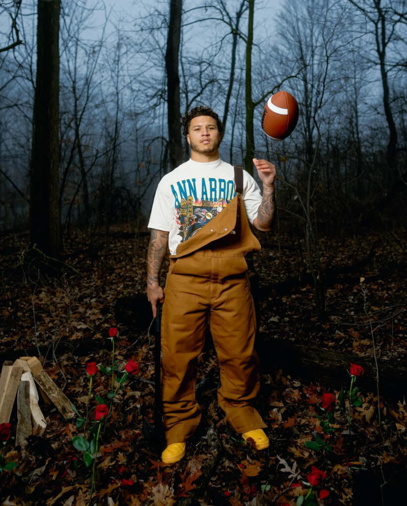 Blake Corum spinning football in misty woodland with fallen leaves and blooming red roses wallpaper