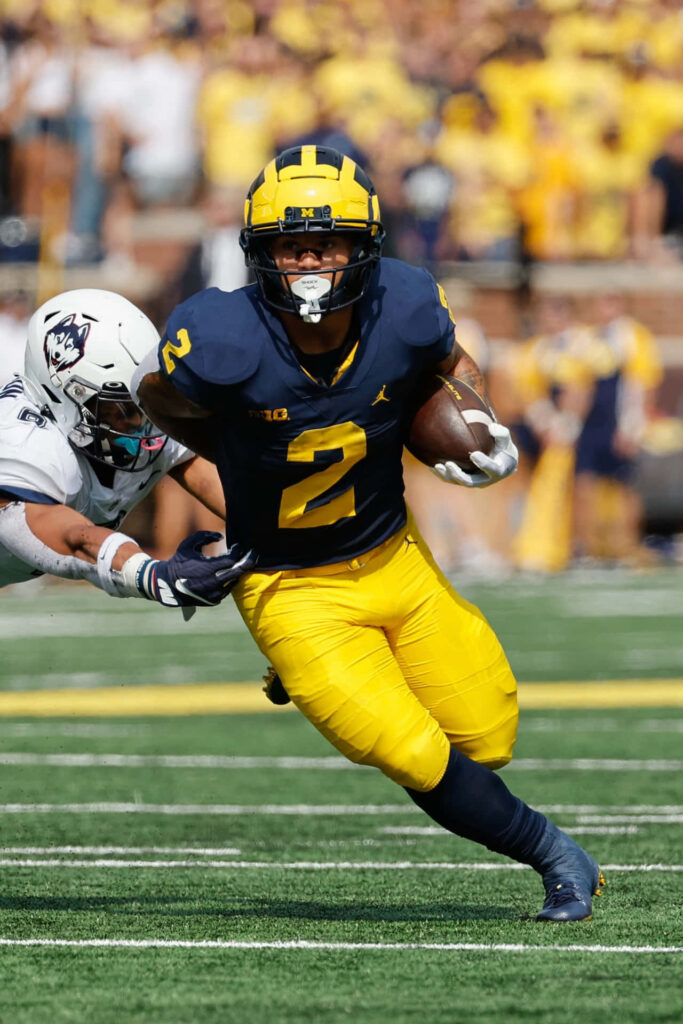 Blake Corum running fast breaking tackle in Michigan Wolverines football game action shot Wallpaper
