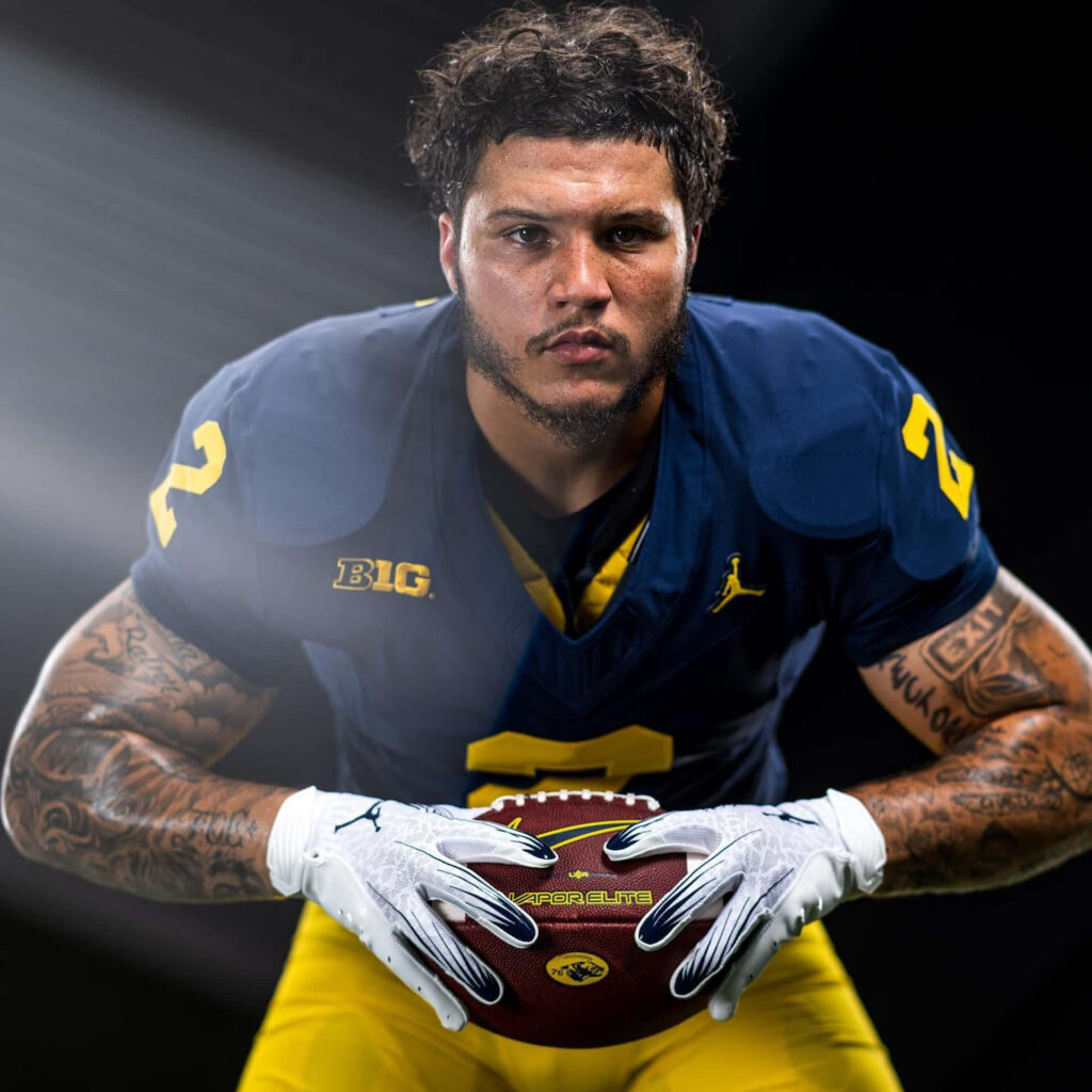 Blake Corum intense portrait in Michigan Wolverines uniform holding football dramatic lighting Wallpaper
