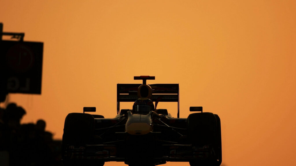 The Excitement Unleashed: An Enthralling F1 Race Acre's Silhouette Painted on a Vibrant Orange Canvas Wallpaper