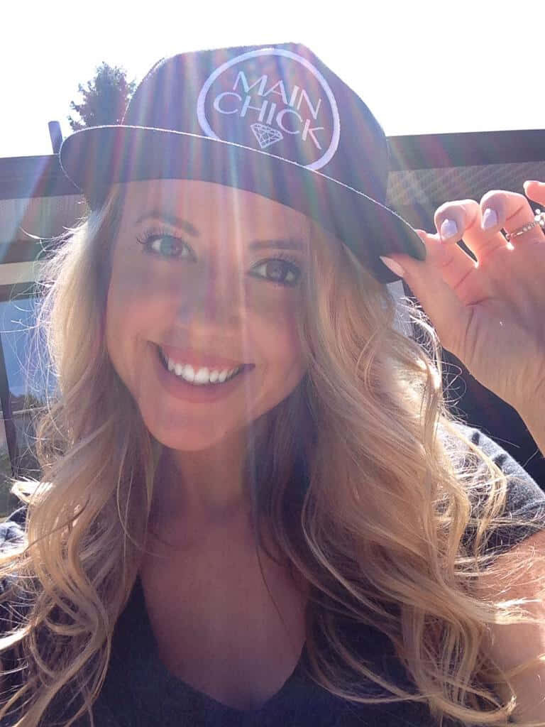 Blonde Chelan Simmons smiling brightly wearing a Main Chick cap in sunlit vibrant wallpaper