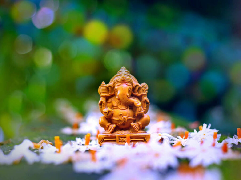Majestic Ganesha Embraced by Nature's Palette - Enchanting Snapshot of a Petite Brown Deity Amidst White Blossoms Wallpaper