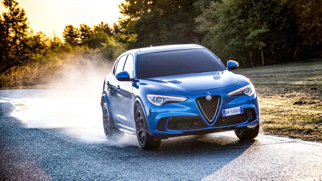 Blue Alfa Romeo Stelvio speeding on scenic sunlit road with natural landscape backdrop wallpaper