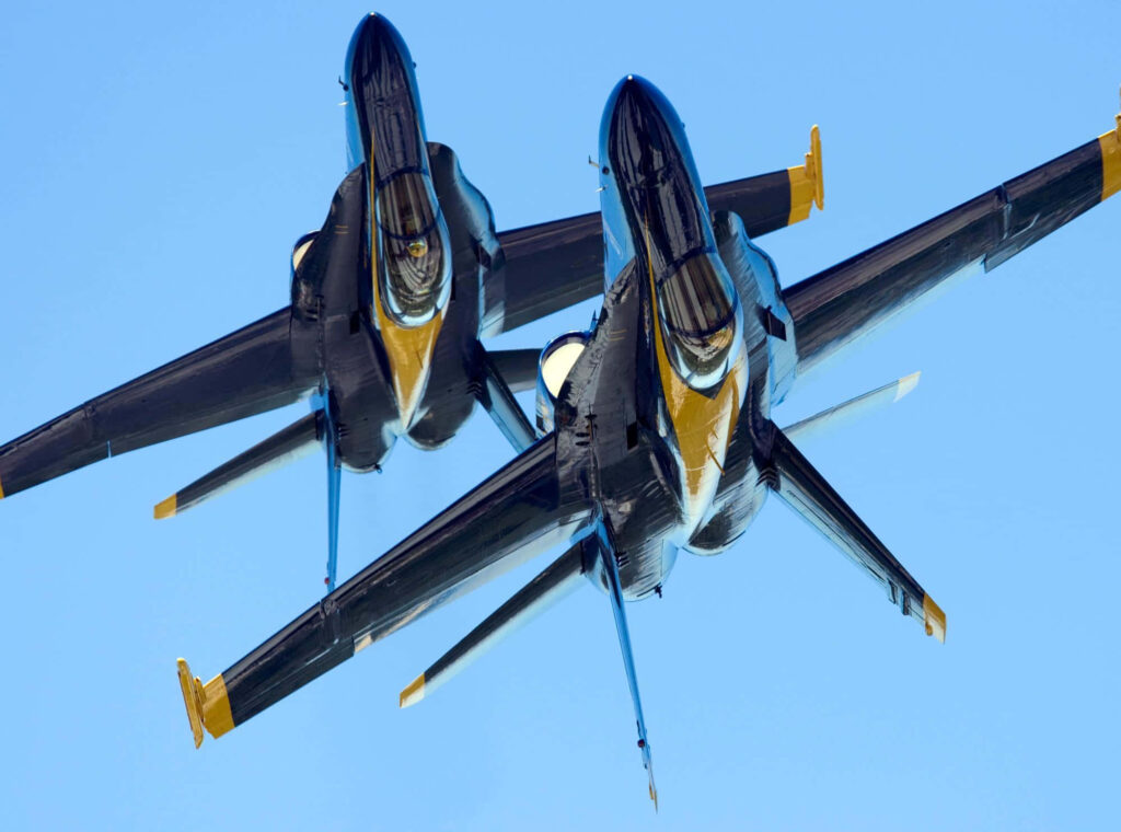 Two Blue Angels fighter jets in tight formation flying against clear blue sky wallpaper background