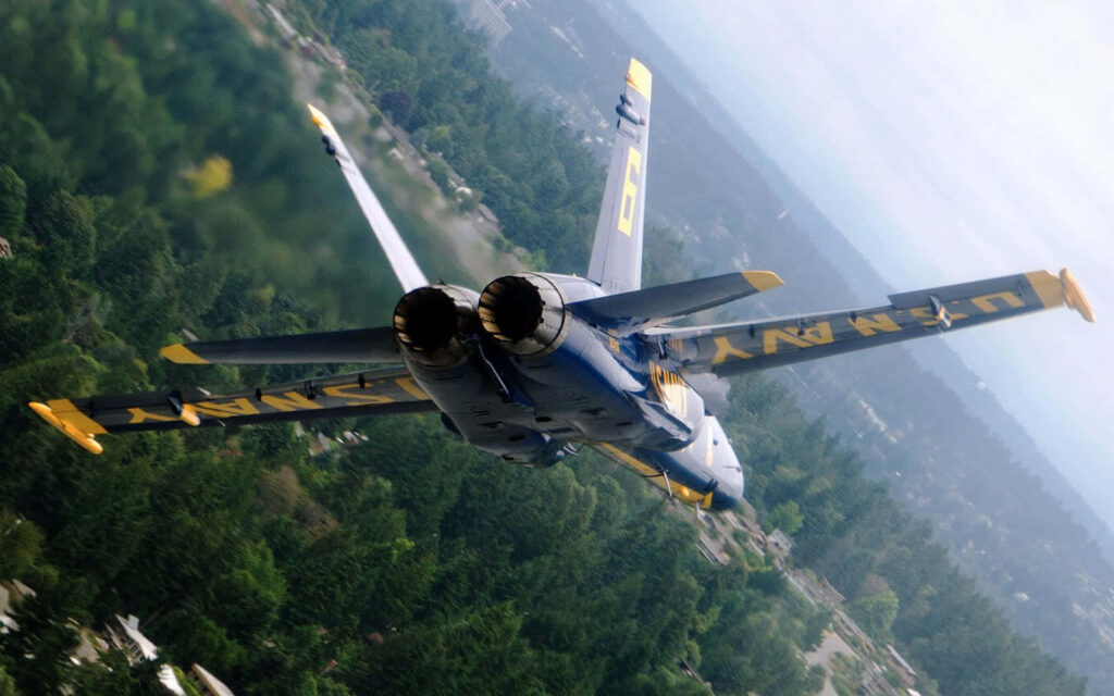 Blue Angels jet soaring over green landscape showcasing US Navy precision and speed wallpaper