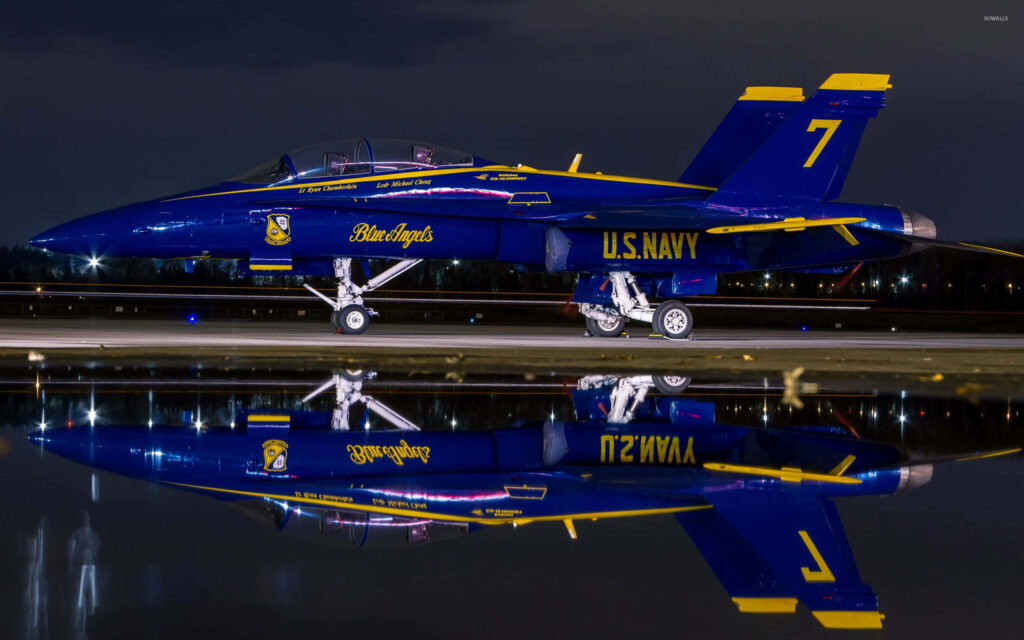 Blue Angels jet with vibrant blue and yellow colors reflected on water at Florida Beach Airshow night Wallpaper