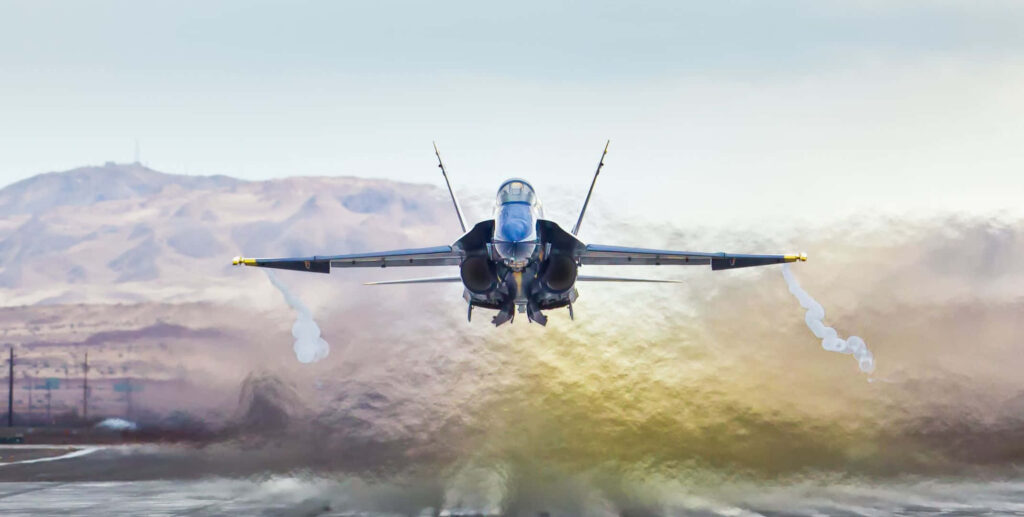 Blue Angels jet soaring from runway with smoke trail and mountains in vibrant sky background Wallpaper