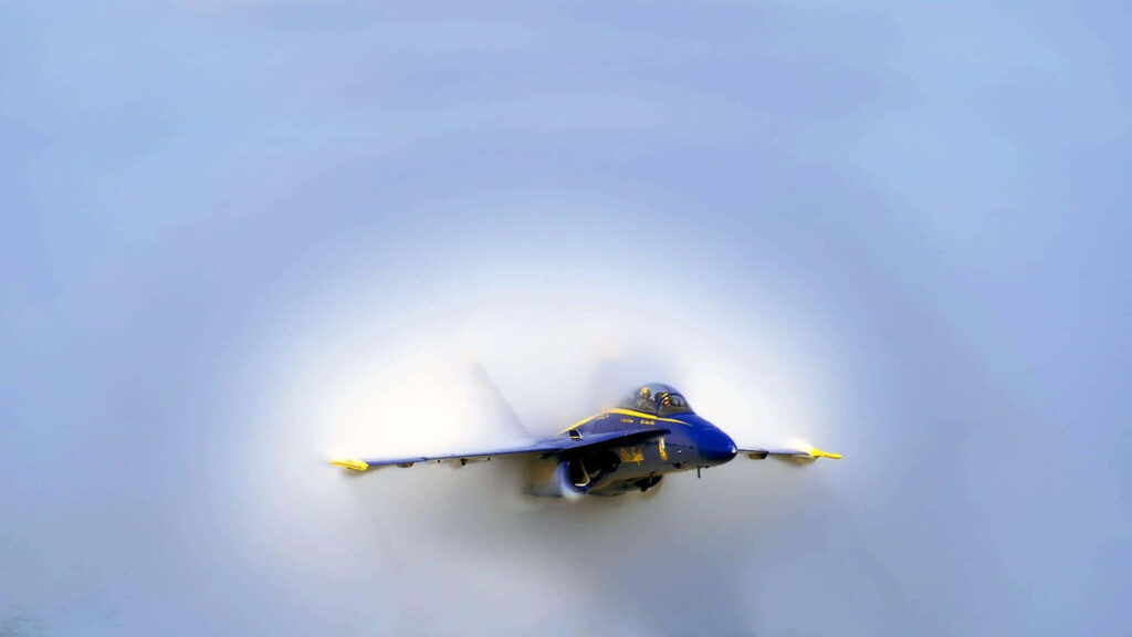 Blue Angels jet in mid-flight with blue and yellow details against misty white sky background Wallpaper