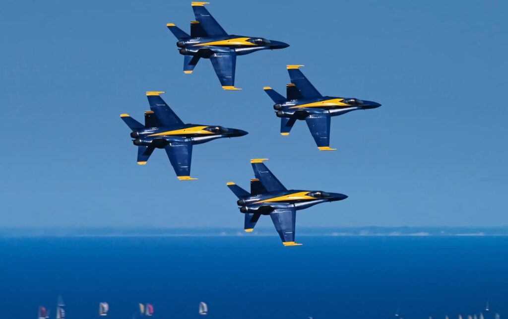 Four US Navy Blue Angels jets in precise formation over ocean clear blue sky wallpaper background