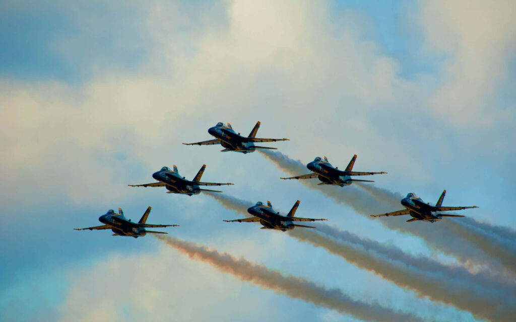 Blue Angels jets flying in close formation with colorful trails against soft cloud sky background Wallpaper