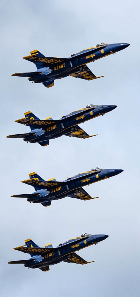 Four Blue Angels jets in tight formation soaring through cloudy sky showcasing precision teamwork Wallpaper