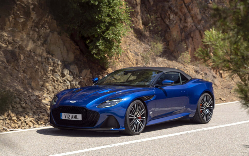 Blue Aston Martin DBS Superleggera cruising scenic road showcasing dynamic design and power Wallpaper