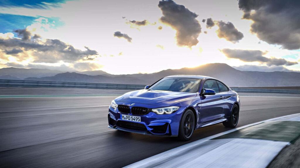 Blue BMW M4 Coupe racing on track with scenic mountains and dramatic cloudy sky background Wallpaper