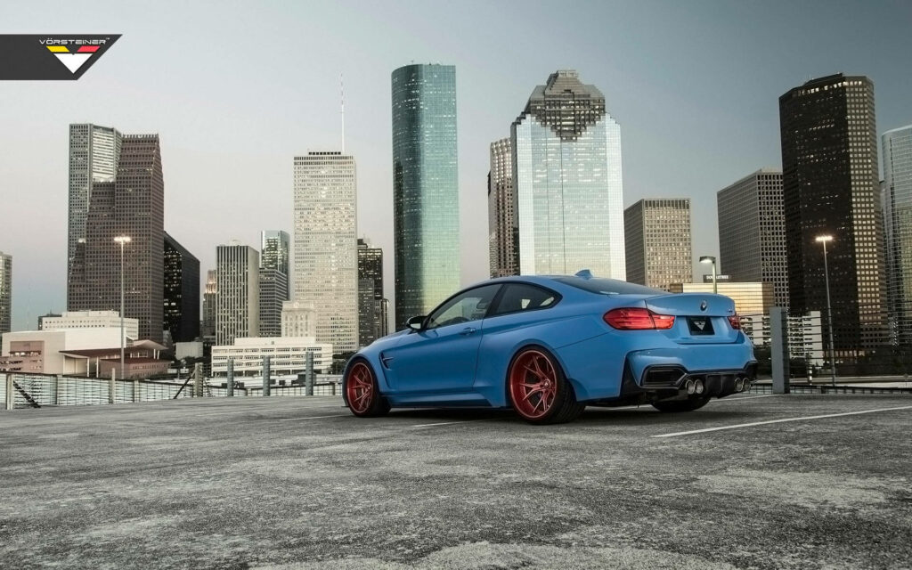 Boldly Parked: Blue BMW M4 GTRS4 Stands Out Against Towering Skyscrapers with Fiery Red Wheels Wallpaper