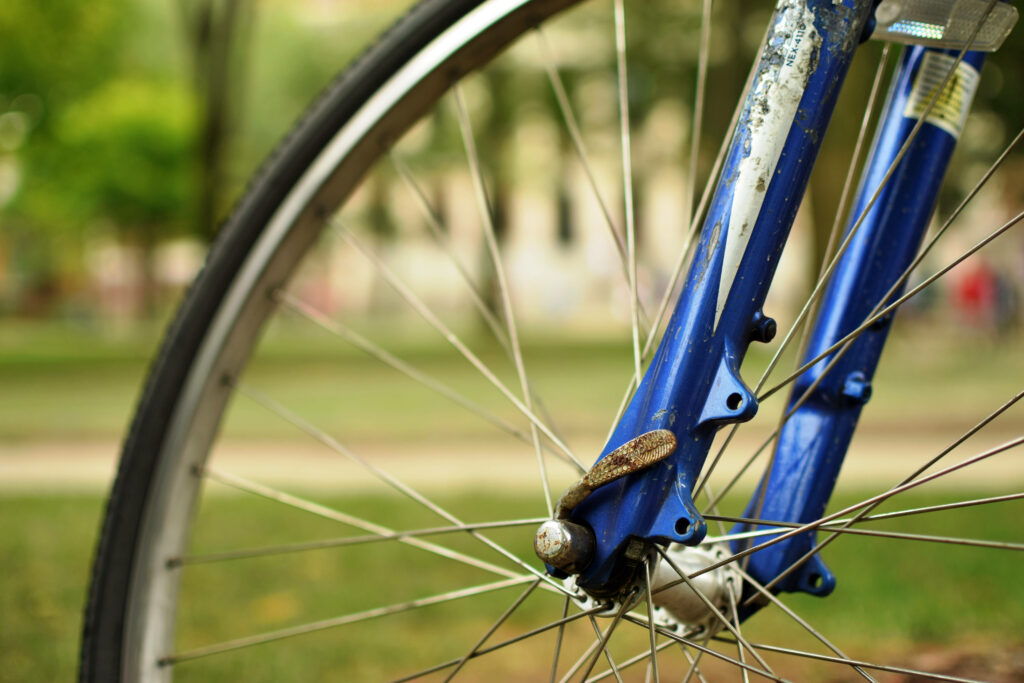 Close-up of blue bicycle wheel spokes and metal frame with blurred green outdoor background Wallpaper